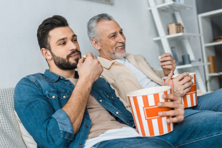 elderly man with adult child watching TV and eating popcorn